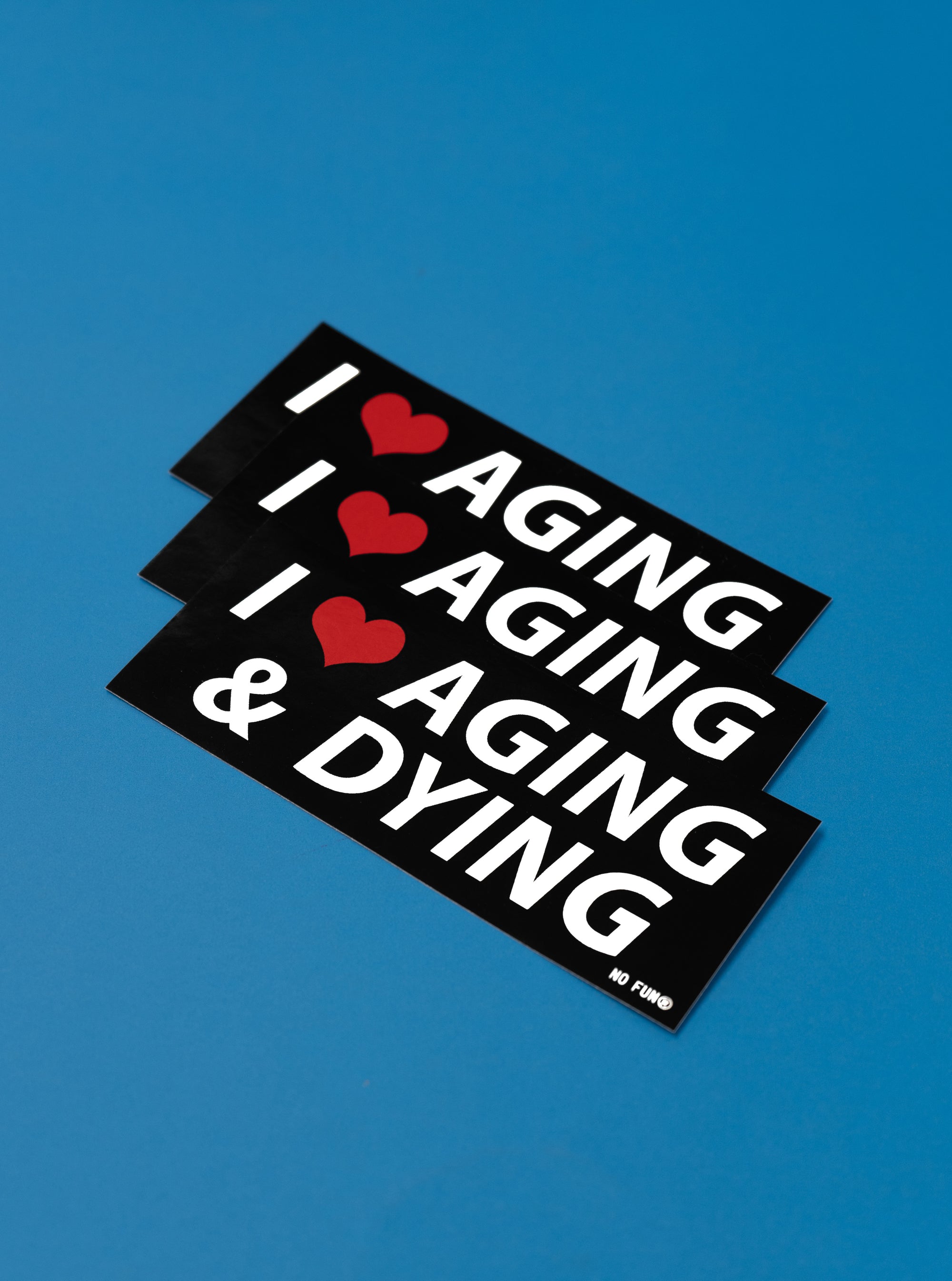 Three "Aging and Dying" Black bumper stickers in a row, slightly overlapped.