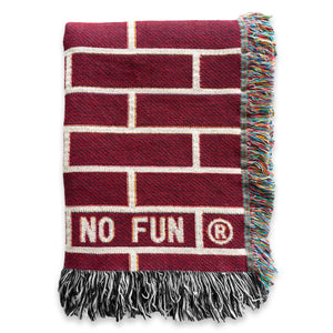 The "Brick" Woven Blanket by No Fun®. The blanket features a red and cream brick pattern that spans the entire blanket. There is a No Fun® logo found in the bottom right hand corner of the product.  Image shows the blanket folded, to better showcase the logo.