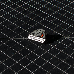 The No Fun Press "Confident Dog" lapel pin on a black cutting-mat.