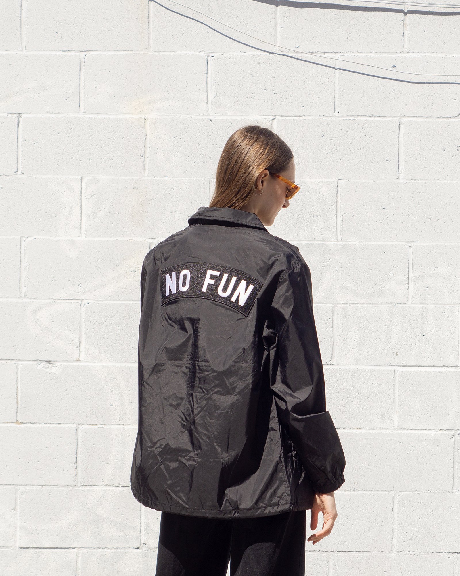 Photo of a female model wearing the "NO FUN®" X "Crawling Death" collaboration coaches jacket.  The model is showcasing the extra large "NO FUN®" logo back patch which is found on the back of the jacket.