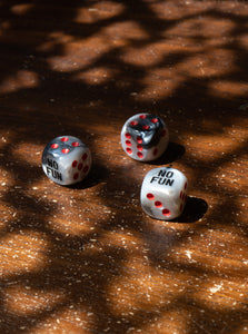 The "No Fun®" Dice Set rolled onto a wooden table.  Shadows are cast across the dice.
