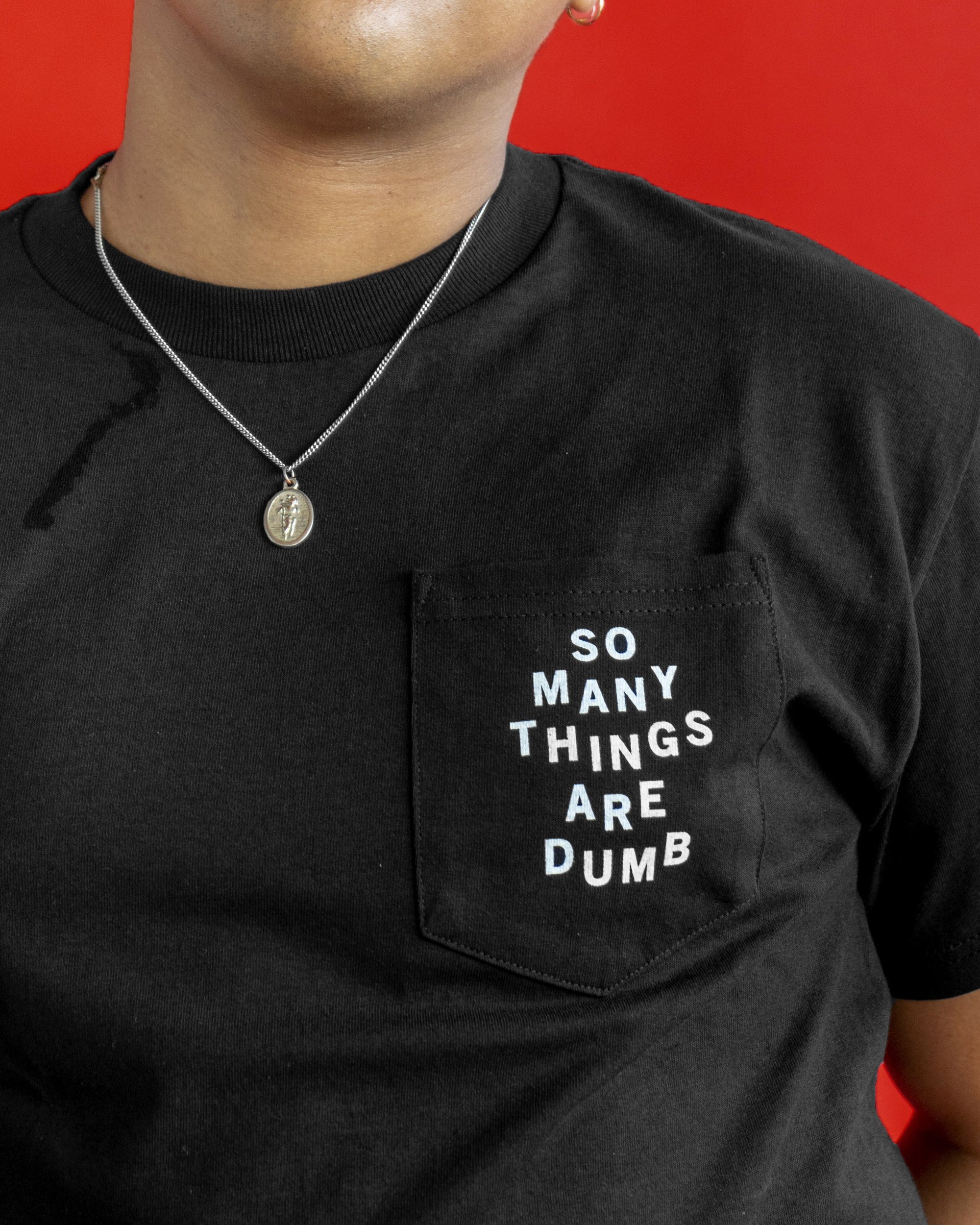 A male model wearing the original NO FUN® "So Many Things Are Dumb" Pocket tee, designed and printed in Toronto. T-shirt features front pocket and white text that reads "SO MANY THINGS ARE DUMB".