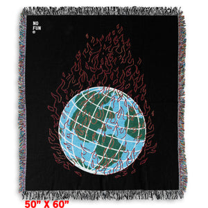The "Global Warming" Woven Blanket by No Fun®. The blanket is black, and features a globe in the center engulfed in flames. The globe is blue and green, and the flames are red. There is a small "No Fun®" logo found in the top left hand corner of the product.