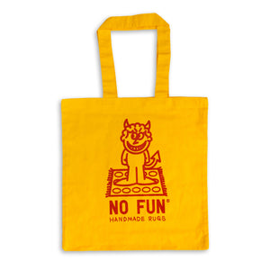 The "Handmade Rugs" Tote Bag by No Fun®.  Tote bag is yellow, and features a print of a devil character standing on a rug.  The phrase "No Fun® Handmade Rugs" is printed below the devil character.
