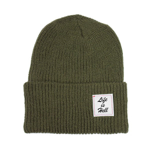 Photo of the "Life is Hell" Beanie by No Fun®.  Product is photographed against a white background.  Beanie is Olive Drab in colour, and features a small white woven label on the cuff that reads "Life Is Hell".  Label is white, with black text, and red contrasting stitching.