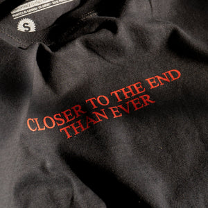 Detail photo of our original "Closer" t-shirt.  T-shirt is black with red chest print that reads "CLOSER TO THE END THAN EVER"..  Based off of posters put up in our neighbourhood warning people about No Fun®.