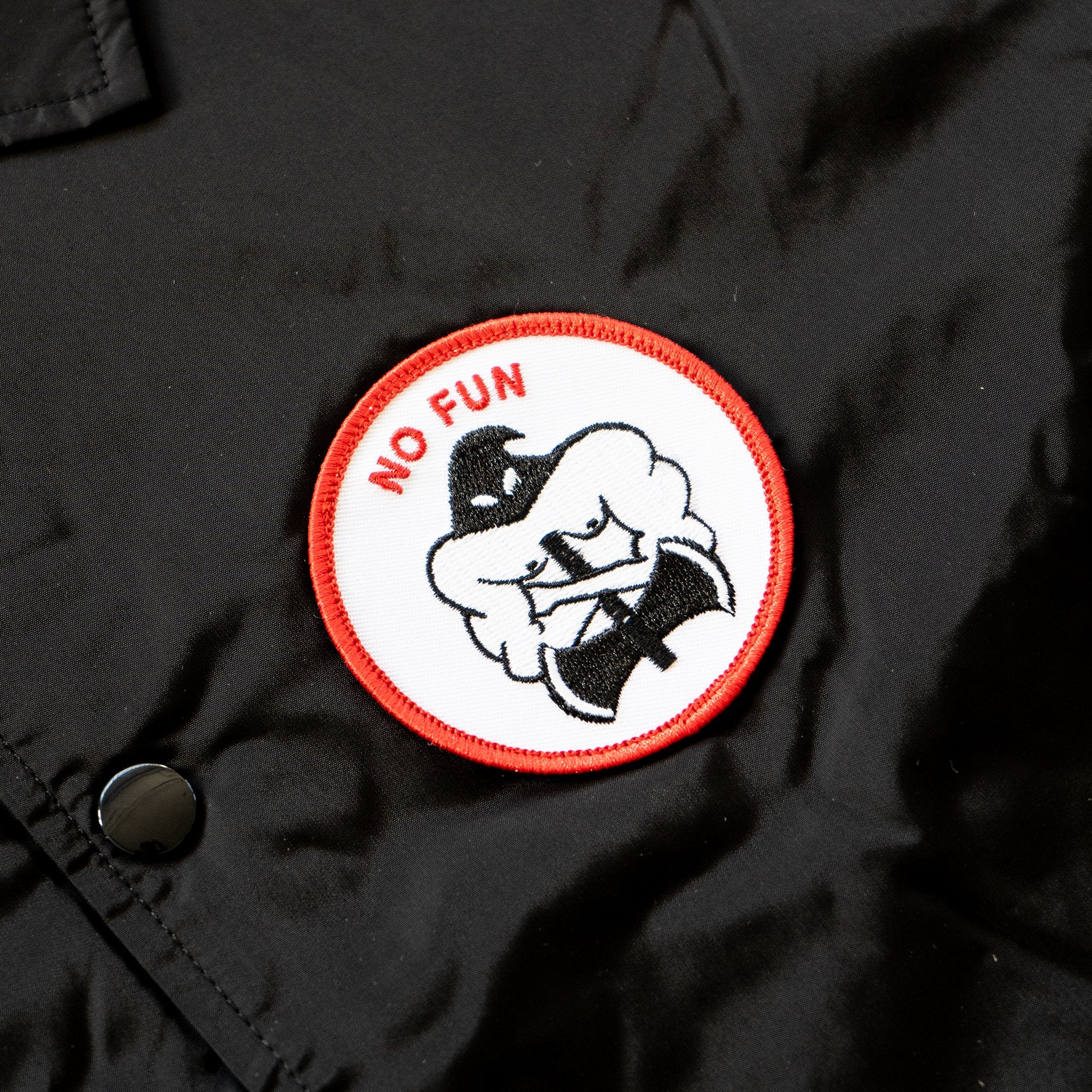Close up image of the black, red, and white executioner patch that is found on the breast of the "NO FUN®" X "Crawling Death" jacket.  The patch also features a red "NO FUN®" logo.  This detail image also showcases the snap button closure.