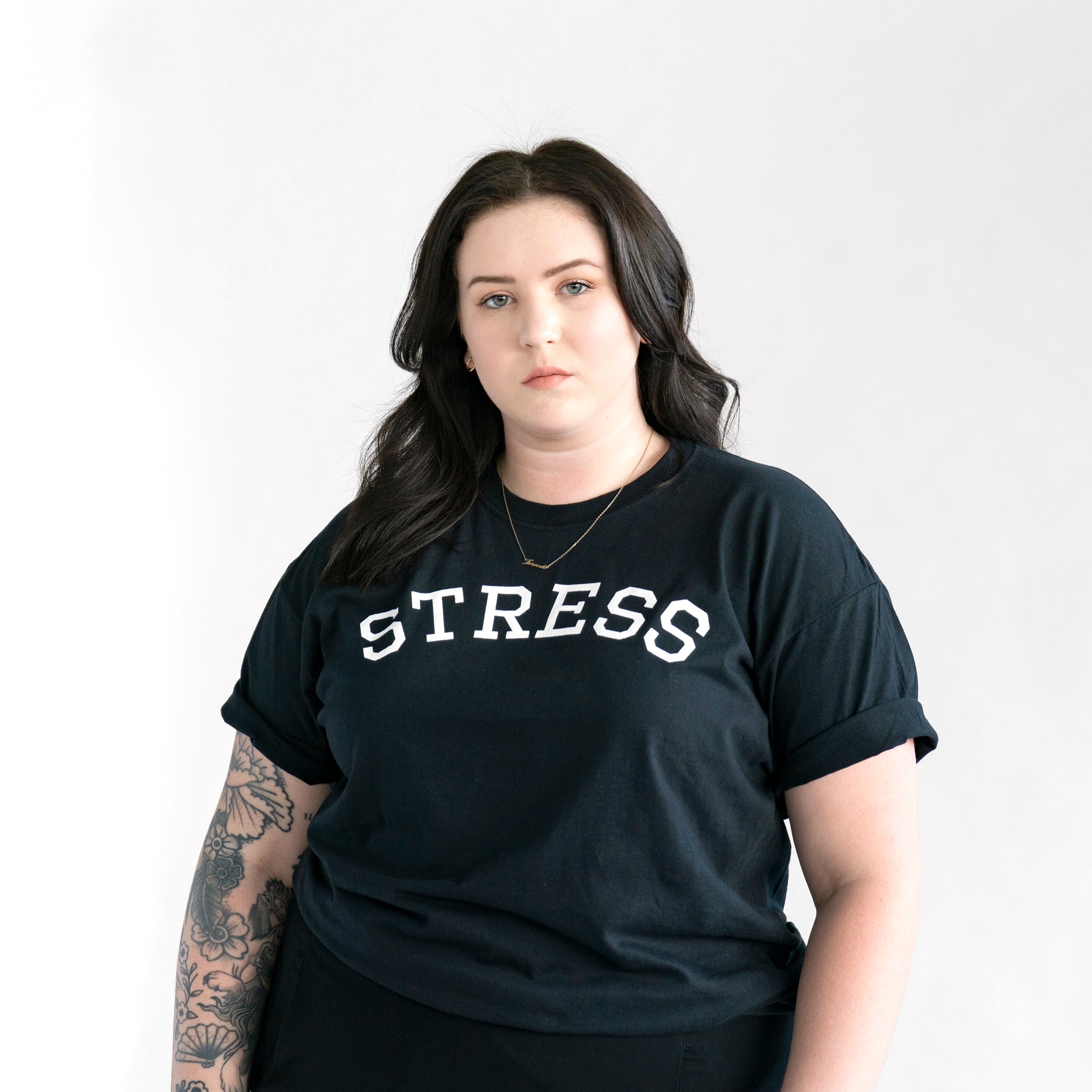 Photo of a female model wearing the original NO FUN® "STRESS" t-shirt. Shirt is black and features large white collegiate style text that reads "STRESS" across the front in an arc shape.