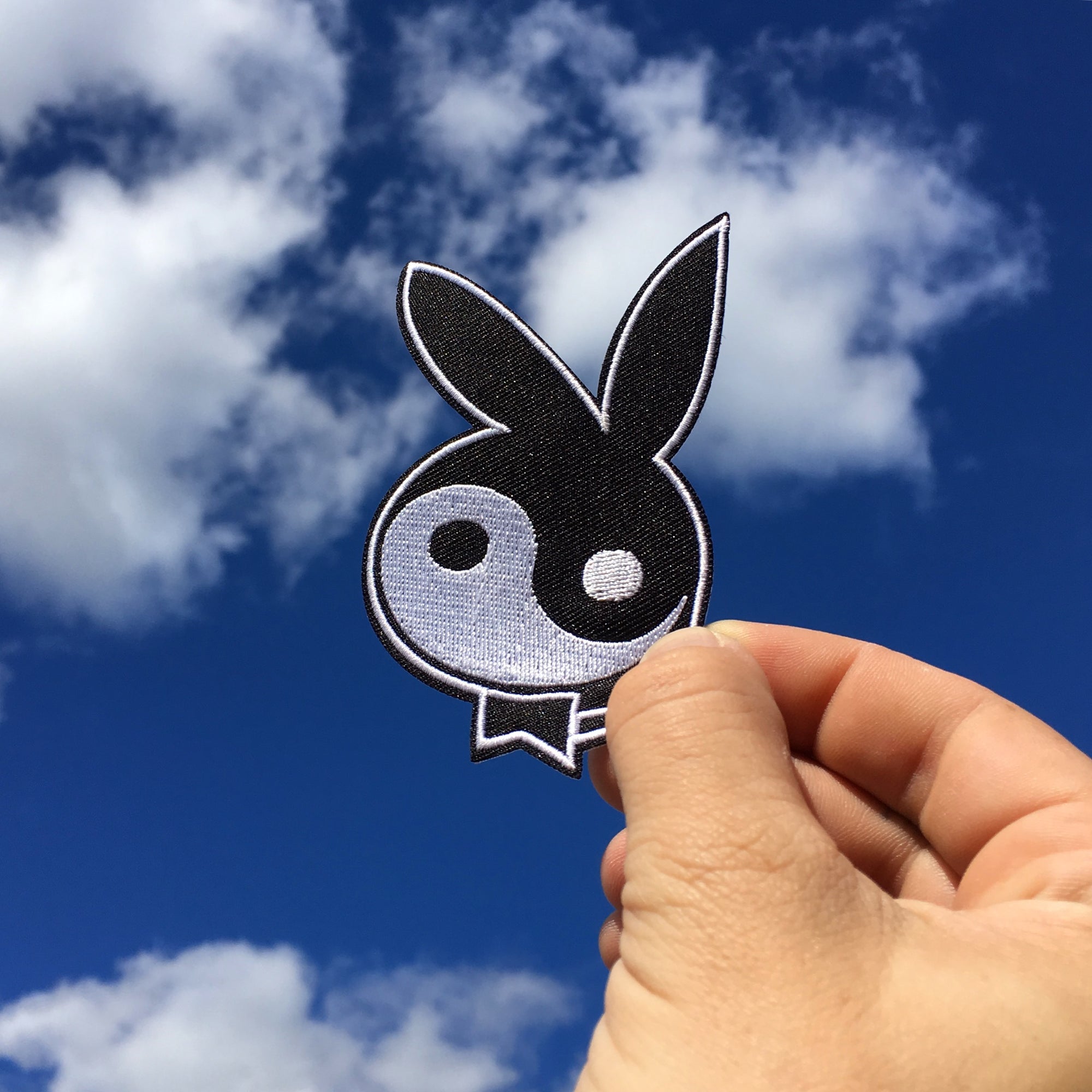 No Fun Press - original "yin yang bunny" embroidered iron-on patch held up against the sky.