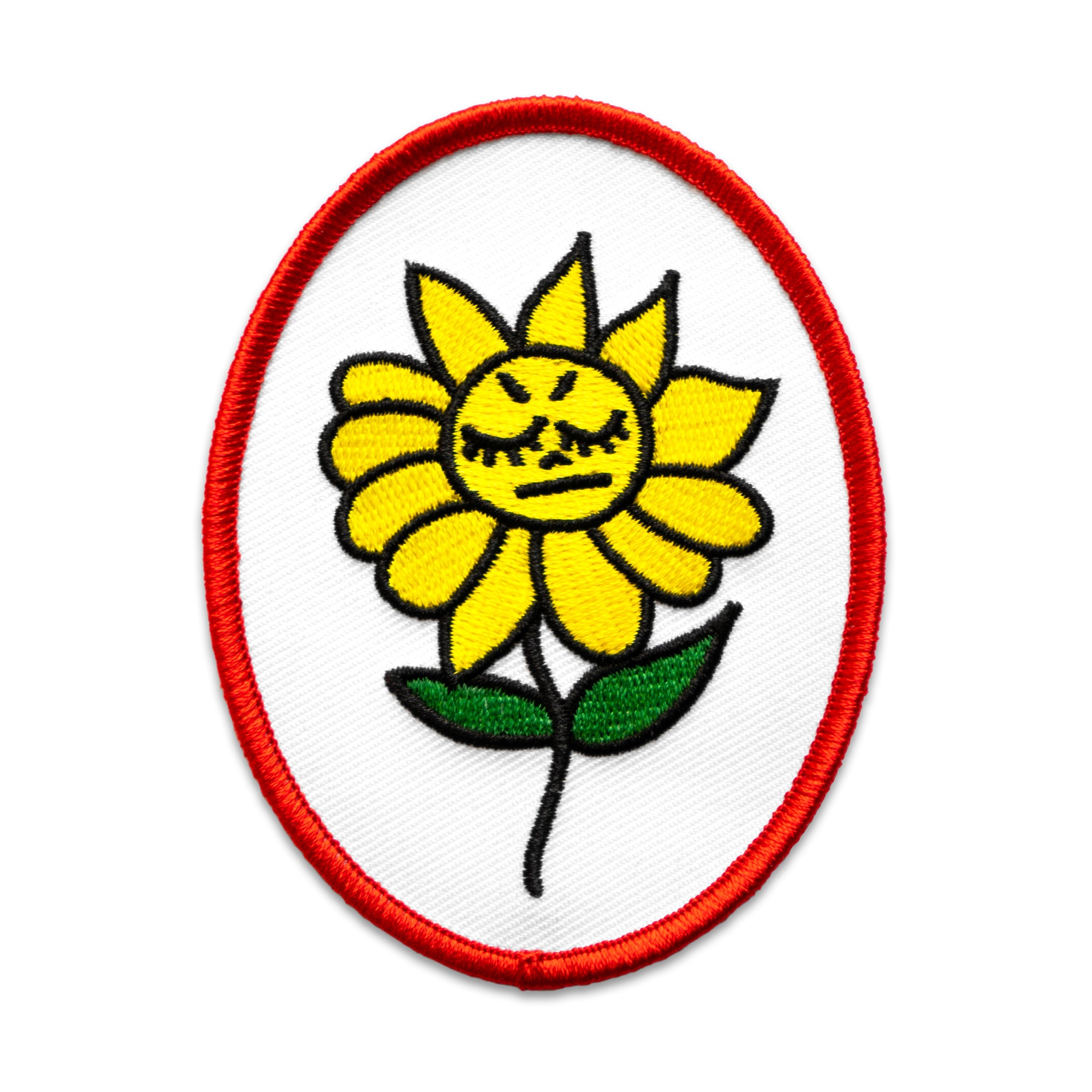 The "Angry Flower" Patch by "No Fun®.  The patch is white, with a red boarder, and is in the shape of an oval.  There is a yellow cartoon flower in the center of the patch.  It has an angry face and two green leaves.