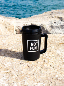 Photo is of the "Big Sipper" Mug in black by No Fun®.  The mug is sitting on top of a large stone, and a lake can be seen behind it. 