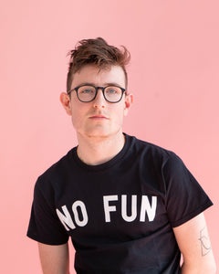"No Fun®" T-shirt being worn by a male model.  He is also wearing glasses, and has visible tattoos.  He is photographed in front of a pink background.