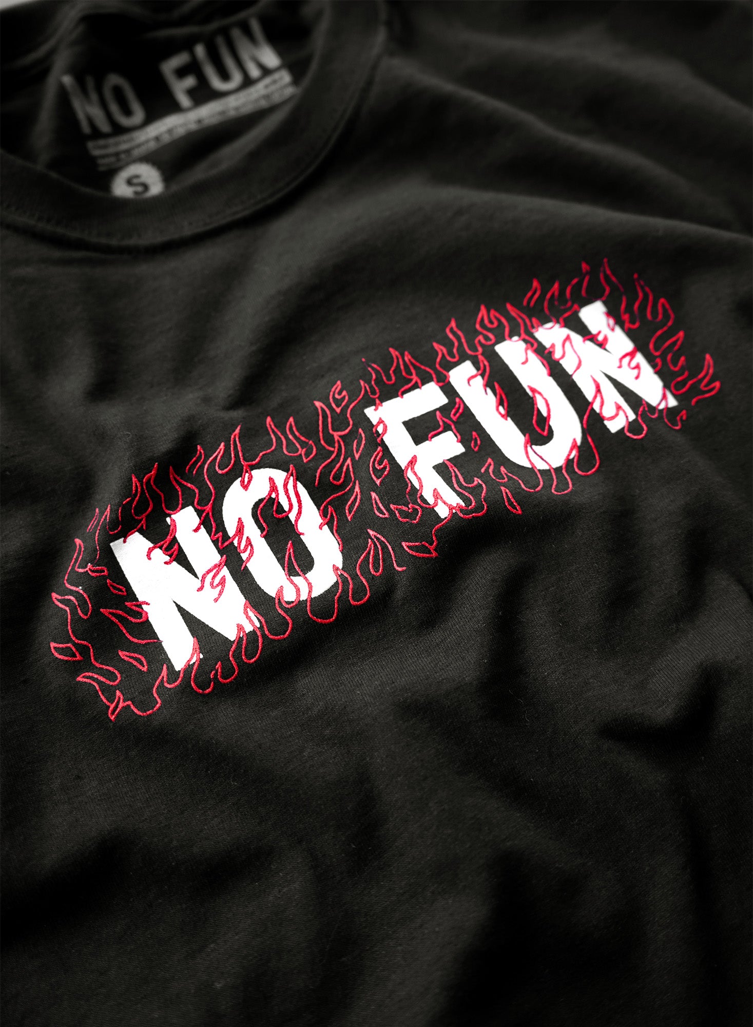 Detail photo of "No Fun®" "Fire" T-shirt.  The t-shirt is black, and features a white "No Fun®" logo surrounded by red linework flames. The graphic is in the center, on the front of the t-shirt.