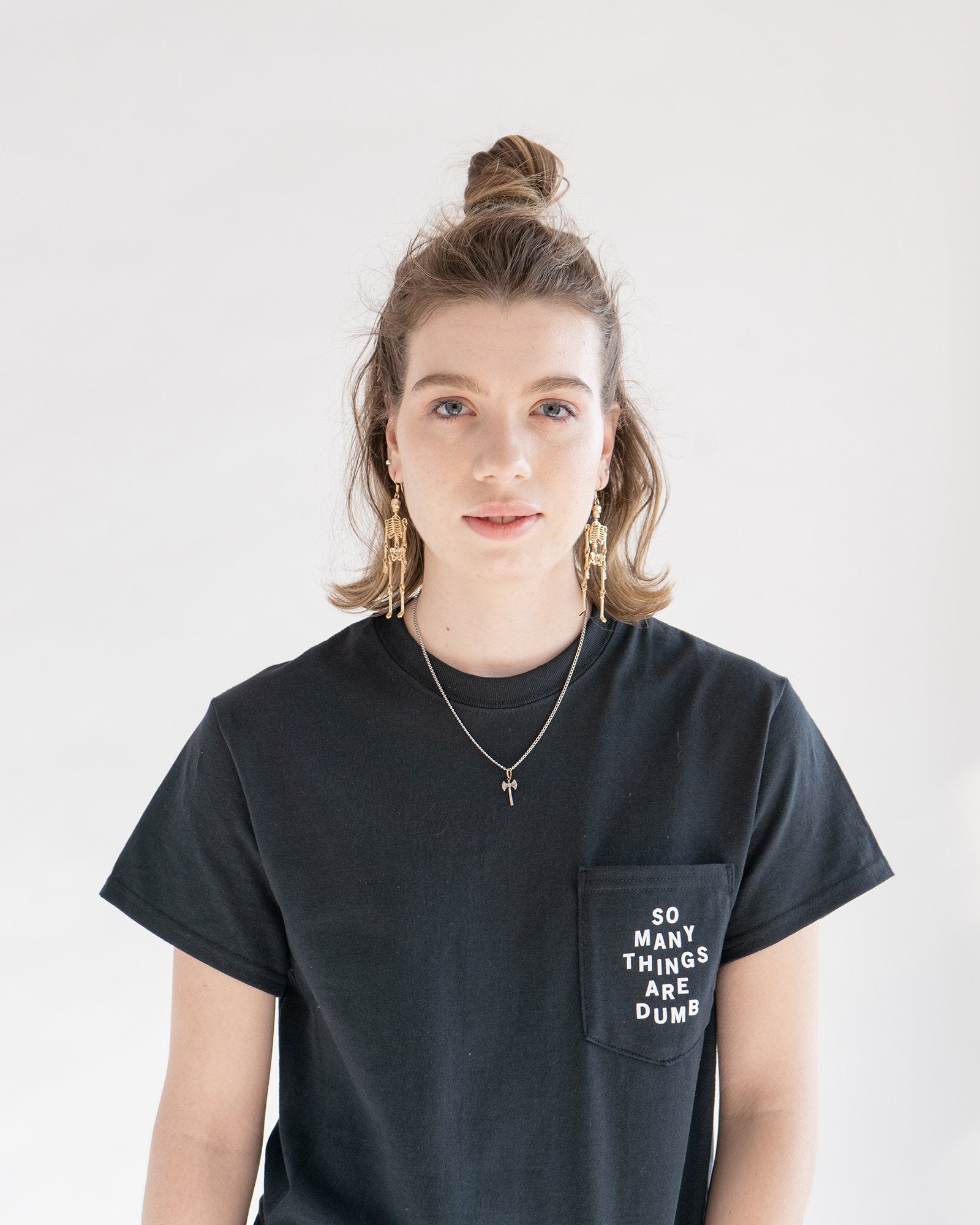 A female model wearing the original NO FUN® "So Many Things Are Dumb" Pocket tee, designed and printed in Toronto. T-shirt features front pocket and white text that reads "SO MANY THINGS ARE DUMB".