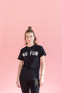 "No Fun®" T-shirt being worn by a female model.  She is also wearing black leggings and has her hair up in a bun.  She is standing in front of a pink background.