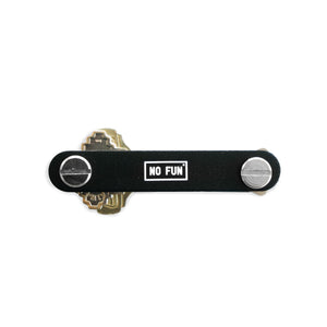 Photo features the "No Fun®" key holder against a white background.  The product is black, with a small white "No Fun®" logo that is found in the enter.  The image showcases 3 keys that have been attached to the key holder on both the left, and right side.