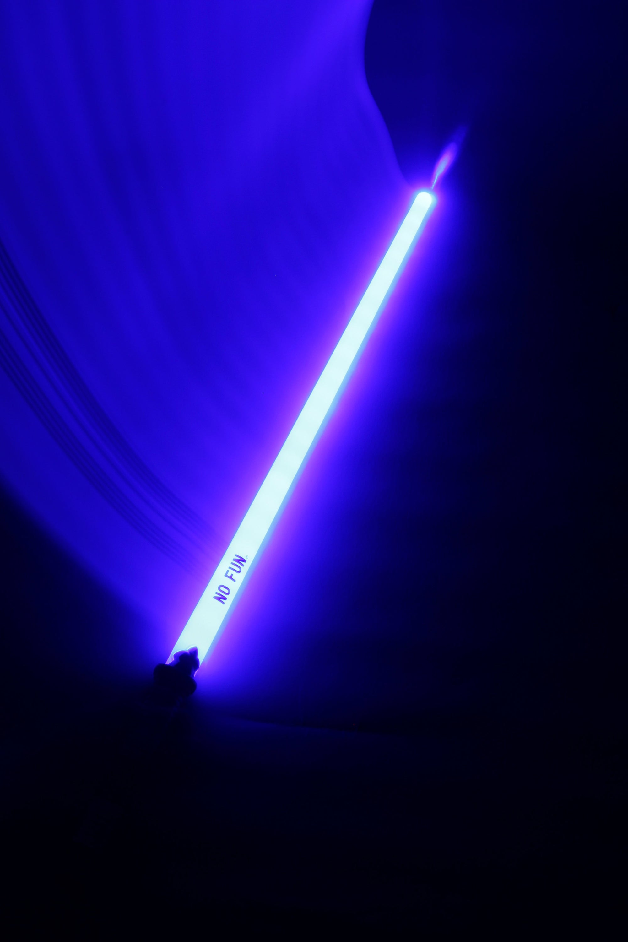 A photo of a blue novelty sword illuminating a dark background.  There is a light trail flowing from the sword to the top left hand corner of the image, showcasing the colour.  The "NO FUN®" logo near the handle is visible to the camera.