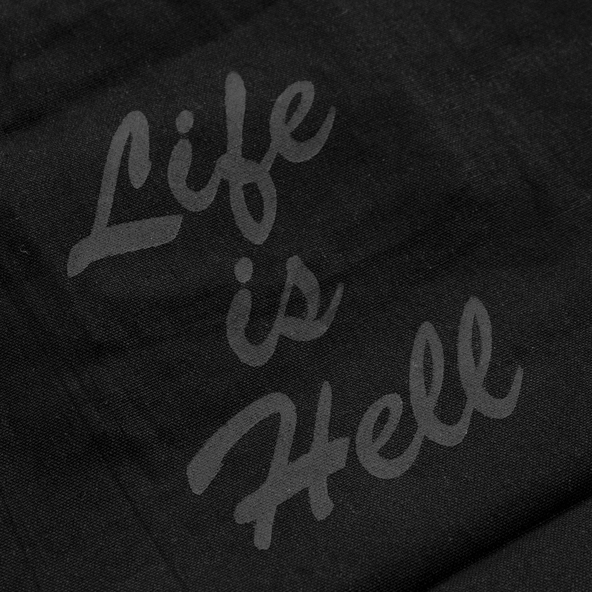 Detail of the "Life is Hell" text on a zippered tote bag.