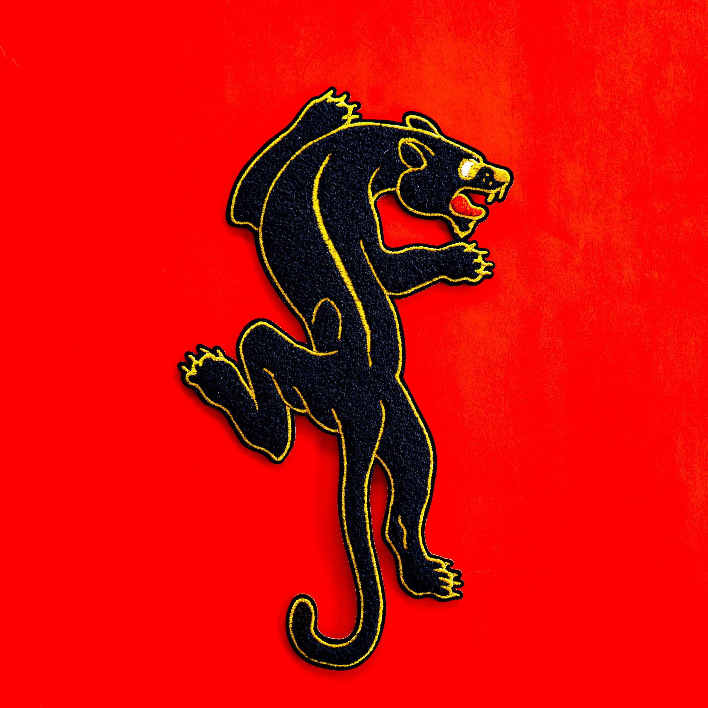 XL Chenille oversized back patch of classic Sailor Jerry style crawling panther. Patch is black chenille with red, and gold embroidery.  The photo shows the patch against a red background, highlighting the chenille texture.