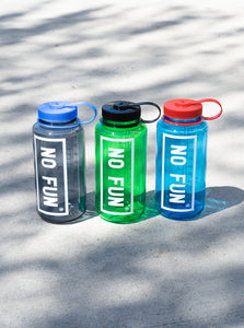 3 colours of the Nalgene® + No Fun® 32oz Bottle.  They are lined up in a row on the concrete.  Shadows of leaves can be seen cast over the bottles.