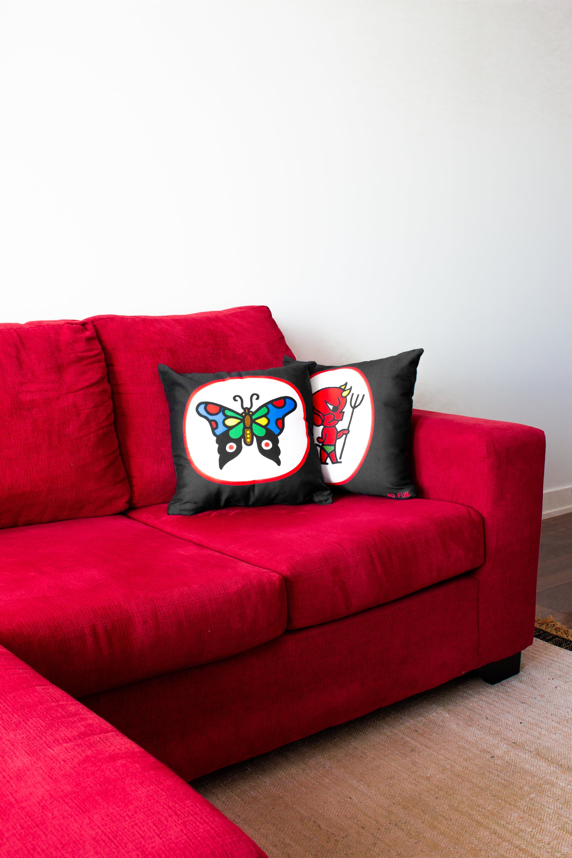The "Devil & Black Widow" Pillow on a red couch.  The room is white, with brown wood floor. 