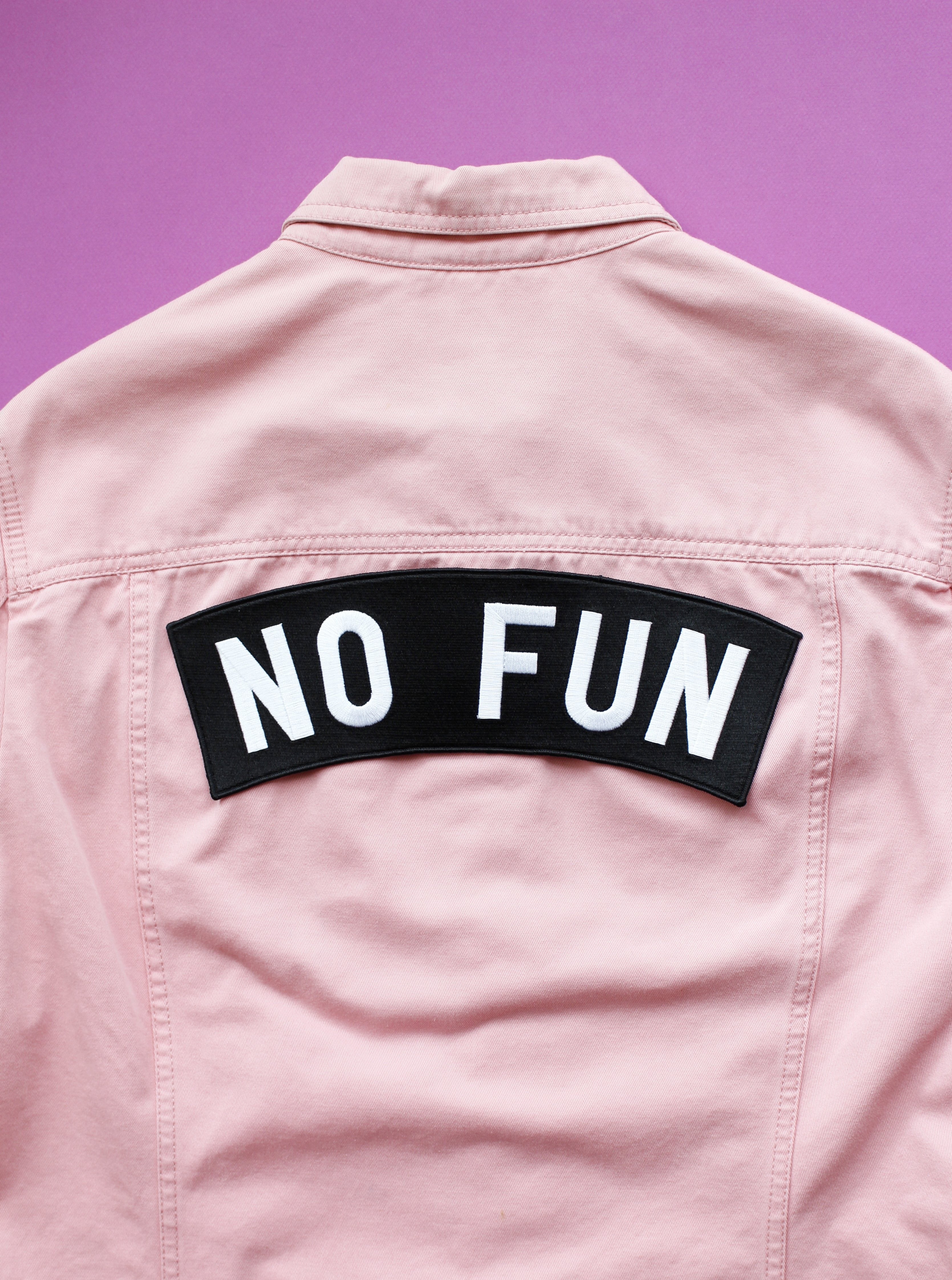 Original "No Fun" XL size rocker embroidered iron-on back patch.  Patch is adhered on a pink denim jacket, set against a purple background.