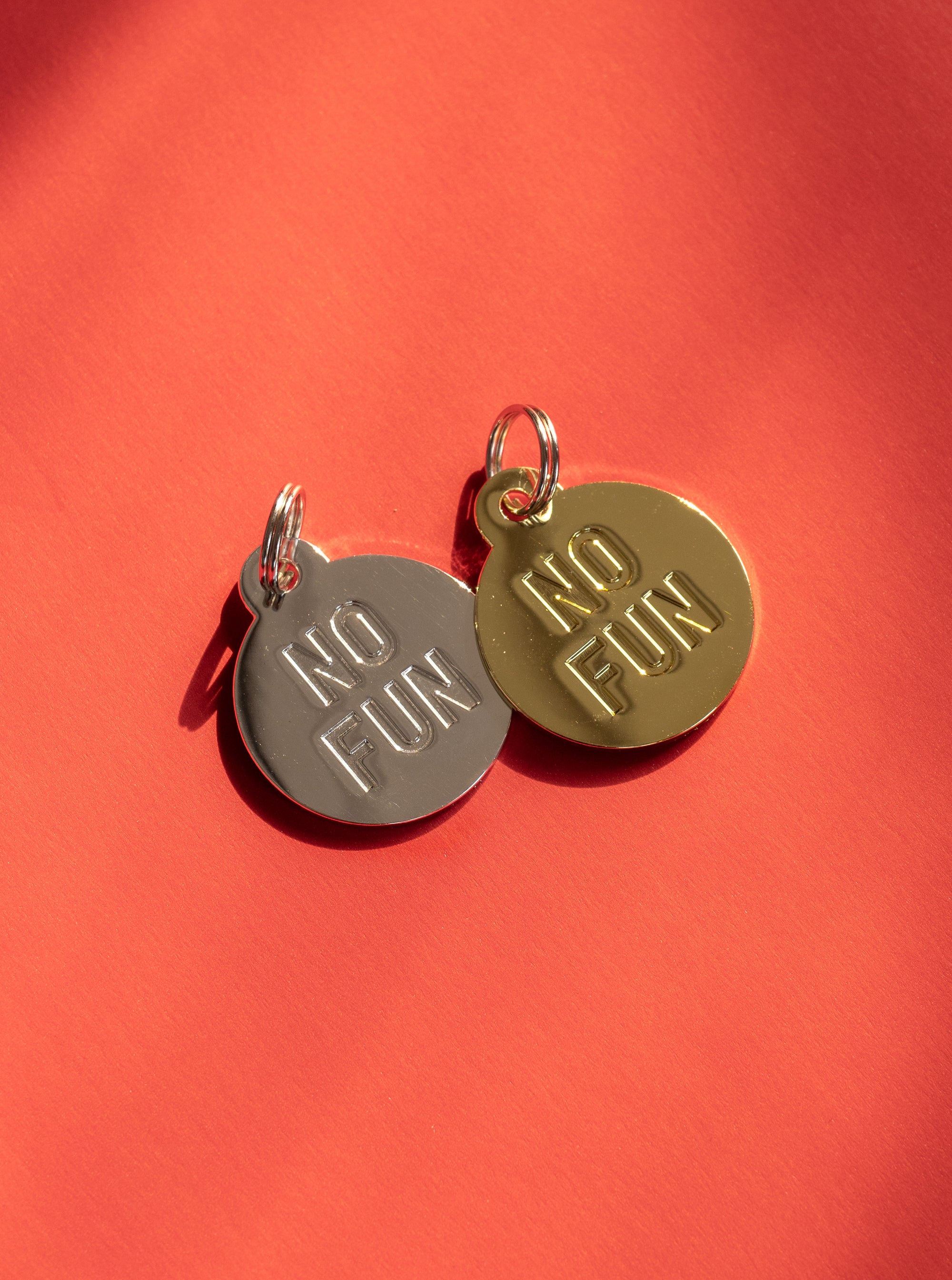 Both colours of the "No Fun®" Pet Tag Keyring against a red background.