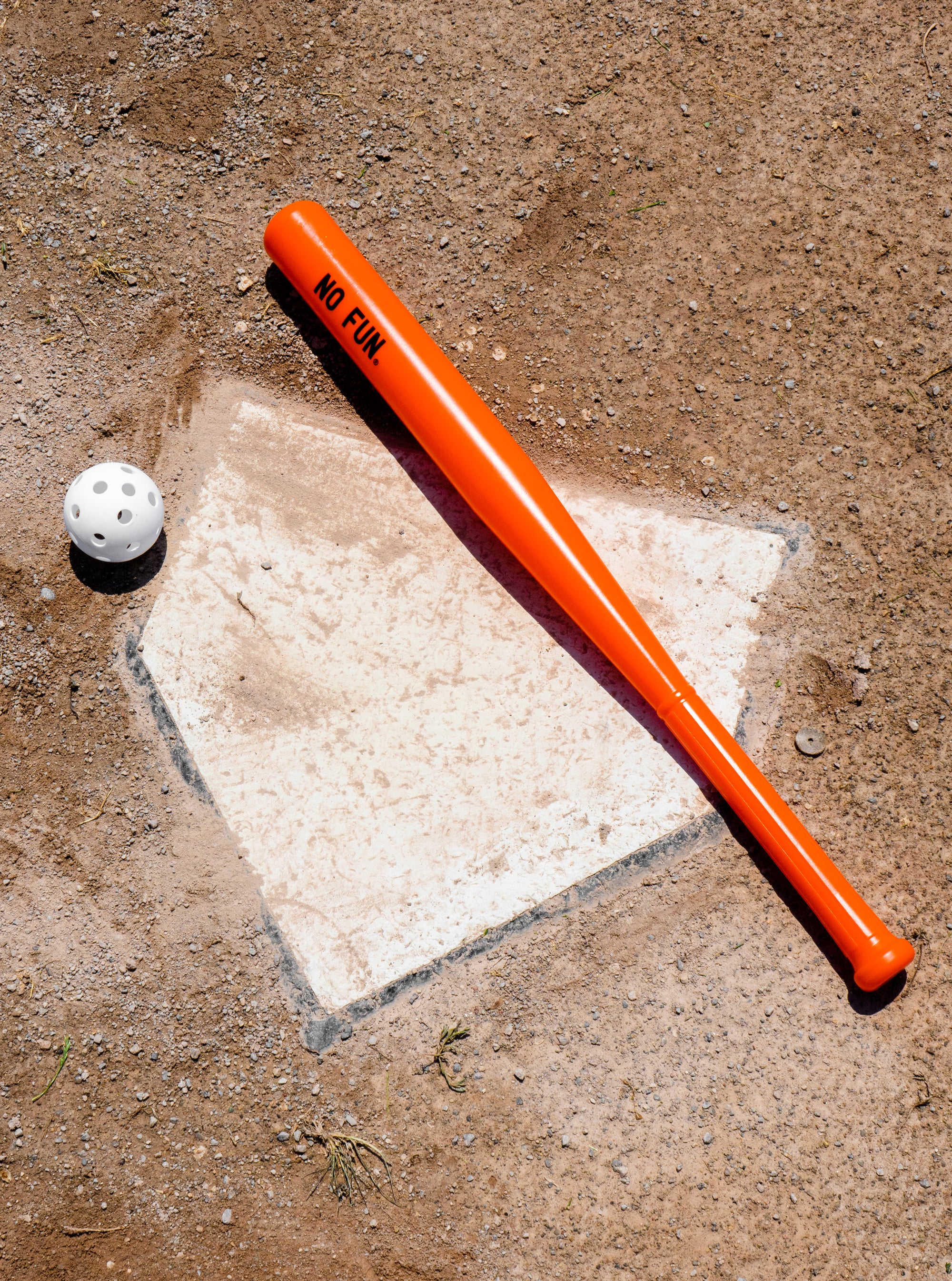 Plastic orange bat with a white ball that has holes laid across home plate.  Looks similar to a wiffle ball and bat set. There is a black No Fun® logo on the barrel of the bat.