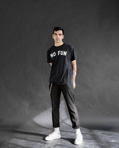 "No Fun®" T-shirt being worn by a male model.  He is also wearing black jeans, white socks, and white shoes.  She is standing in front of a black background.