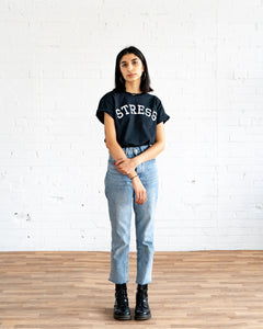 Photo of a female model wearing the original NO FUN® "STRESS" t-shirt. Shirt is black and features large white collegiate style text that reads "STRESS" across the front in an arc shape.