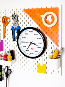 The original "WORK" studio wall clock. Wall clock with "WORK" replacing the hours/minutes on the face. Red No Fun® logo in center.  Clock is photographed on a pegboard, surrounded by various studio tools.